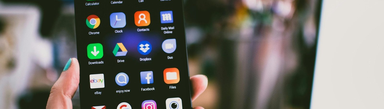 A close-up image of a person's hand holding a smartphone displaying various popular apps.